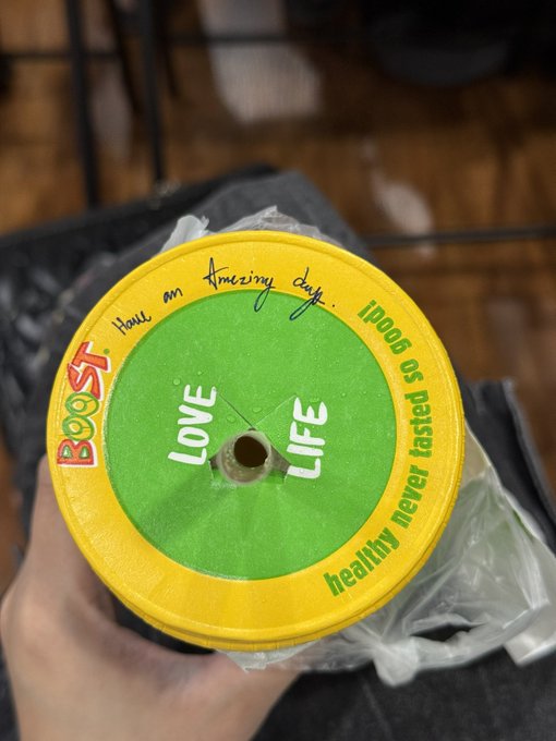 A hand holds a yellow plastic yo-yo with a green center reading 'LOVE LIFE,' with additional text around the rim stating 'BOOST', 'Have an Amazing day.', and 'healthy never tasted as good.'