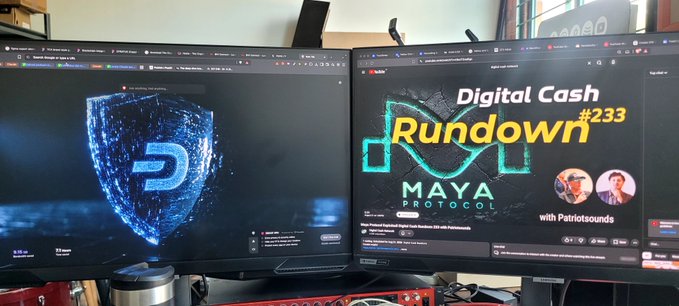 Two computer monitors on a desk; the right one displays a YouTube thumbnail reading "Digital Cash Rundown #233 with Patriotsounds" about "MAYA PROTOCOL", while the left monitor shows a blue "D" shield logo.