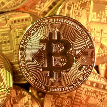 A close-up image of a physical gold Bitcoin coin resting atop other similar gold cryptocurrency coins.