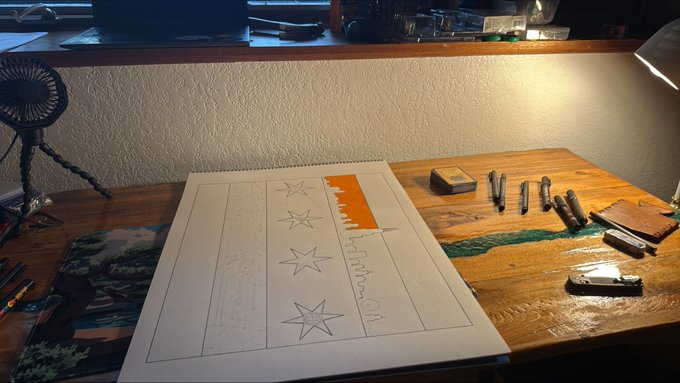 A workspace scene showing a sketchbook on a wooden desk with pencil drawings of stars and the words "Psalm 60," surrounded by drawing tools, markers, and a small fan in the background.