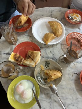 An overhead view of a marble table with plates of pastries, coffee cups, and a bowl of shaved ice dessert, with a person's hand reaching for food.