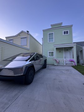 A Tesla Cybertruck is parked in the driveway of a light green two-story home at dusk, complementing the post's mention of the "Robotaxi" (Tesla's autonomous vehicle service) alongside recent NFT, cigar, and Starship launch wins.