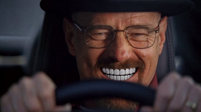 A close-up of the character Heisenberg (played by Bryan Cranston) from Breaking Bad, wearing his black hat and glasses, smiling widely to reveal diamond-encrusted teeth while gripping a steering wheel.