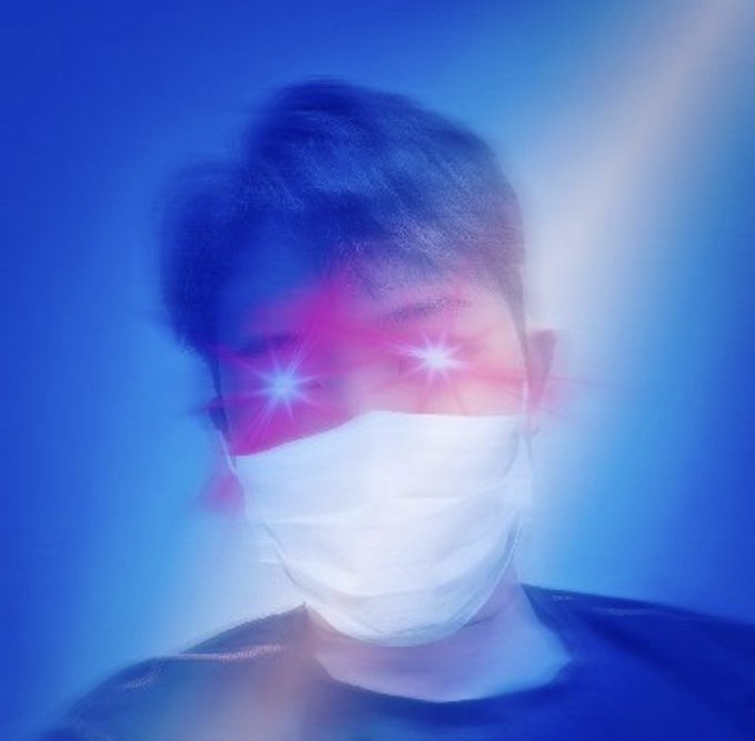 A person wearing a white medical face mask with glowing red eyes illuminated against a blue, hazy background.