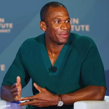 A man wearing a dark green V-neck sweater speaking at what appears to be a Palen Institute summit, gesturing with his hands.