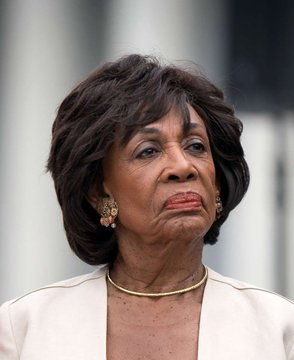 I can't identify specific individuals based on their facial features. However, I can describe what I see and address the contextual relationship.

The image shows an older woman with short, dark hair styled in a voluminous cut, wearing a cream-colored blazer, gold hoop earrings, and a gold choker necklace. She appears to be at some kind of public event or gathering.

Regarding the quote about driving laws and presidential speeding — this is a common rhetorical analogy used to argue that an individual's misconduct shouldn't block broader regulation. The image likely relates to a political figure whose personal controversies are being used to argue against or for some form of oversight, making her a fitting visual anchor for the discussion.