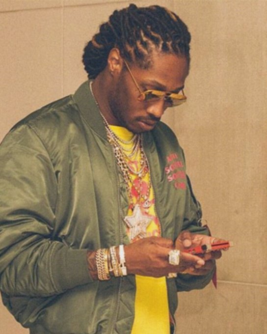A man with braided hair, wearing yellow-tinted sunglasses, a green bomber jacket, and a large star pendant necklace, looks down at his phone while adorned with multiple gold chains and diamond rings. The image, paired with a post referencing "$SEND" and Claude, captures a moment of phone-checking that visually ties to the text's themes of digital communication and staying connected during hard times.