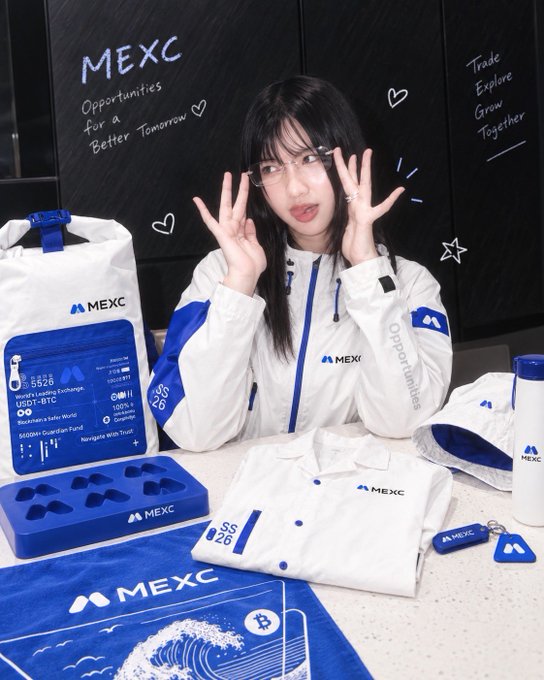 A woman with long black hair and glasses poses with MEXC-branded merchandise, including a white and blue windbreaker with "SS 26" and "Opportunities" printed on it, a matching tote bag, and various accessories, while making a playful face with her hands raised near her eyes. The black backdrop displays "MEXC - Opportunities for a Better Tomorrow" and "Trade Explore Grow Together" alongside decorative hearts and stars, promoting the Fashion Pioneer Ambassador event.