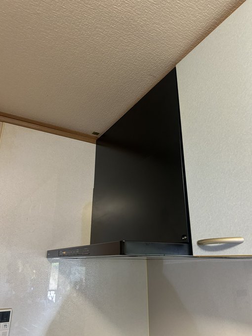 A black range hood mounted under cabinets in a kitchen with a beige ceiling and tiled backsplash.