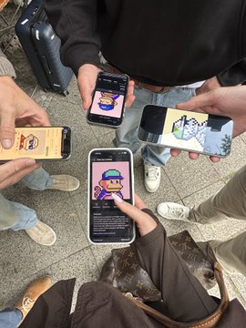 The image shows a group of people standing around each other, with one person holding up their phone displaying an image or video related to Monke brunch Solana Summit in Berlin. The attendees are wearing casual clothing such as jeans and sneakers, suggesting that they might be at a social event or gathering.