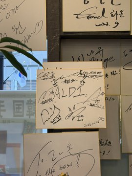 Whiteboards and canvases are displayed near a window, covered in signatures and messages including "Raon Yakiniku," "2024.04.01," "ALDL," and "To 24," commemorating ALD1's visit to the restaurant.