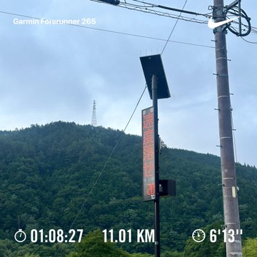 An outdoor view showing a forested hillside with a transmission tower, captured with a Garmin Forerunner 265 displaying metrics: time 01:08:27, distance 11.01 KM, and pace 6'13".