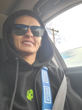 A young man wearing sunglasses, a black hoodie, and a blue "MISHIMOTO" racing harness sits in the driver's seat of a car, smiling at the camera—appearing as the proud owner ("ape") of his vehicle.
