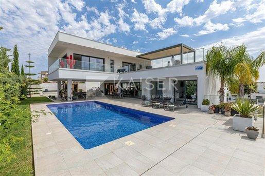 A real estate listing photo of a modern white luxury villa with a swimming pool, palm trees, and outdoor patio furniture, watermarked with 'Kaiser Property'.