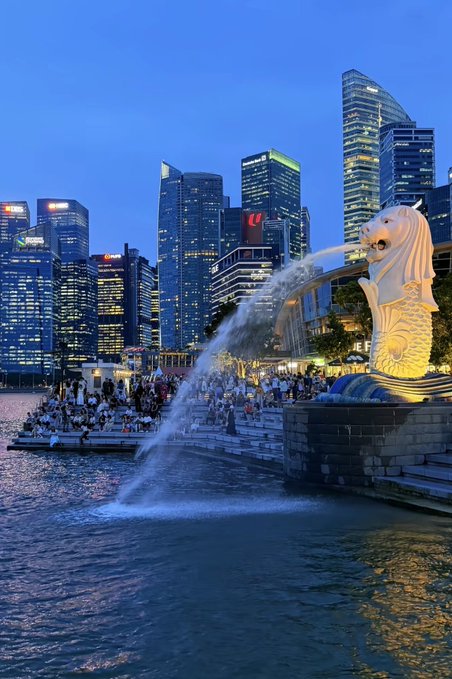 The Merlion statue spouting water at Marina Bay in Singapore with the illuminated city skyline at twilight.