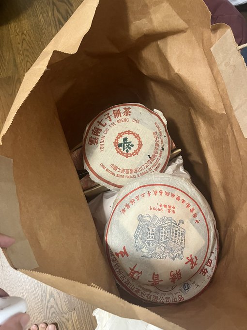 Two rounds of Young Chen Kee Sheng Cha Chinese Pu-erh tea cakes sit in a brown paper bag, labeled with "Young Chen Kee Sheng Cha" and "China National Native Produce & Animal By-Products Import Export Corp," ready to be brewed for the burn.
