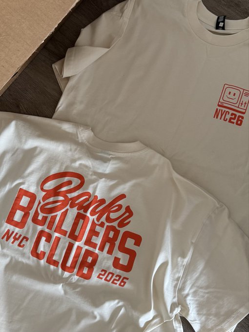 Two cream-colored t-shirts laid out, one featuring a retro computer graphic with 'NYC 26' in red, and the other showing a 'Banker Builders Club NYC 2026' graphic in red.