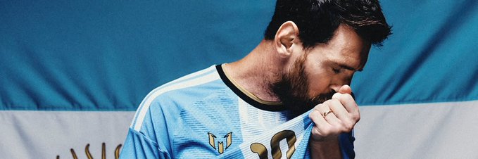 A bearded man in a light blue jersey appears emotional, pulling the collar of his shirt up toward his face, with an Argentine flag design behind him.
