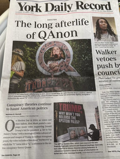 A copy of the York Daily Record dated Thursday, October 9, features the headline "The long afterlife of QAnon" by Matthew N. Hannash, with a photo of a woman wearing a "TRUMP 2020" Q-themed shirt and mentions of the Jeffrey Epstein files and their connection to QAnon theories. The accompanying post aligns with the article's exploration of how QAnon conspiracy theories continue to persist in American political discourse, despite the image's tone suggesting critical analysis rather than endorsement.