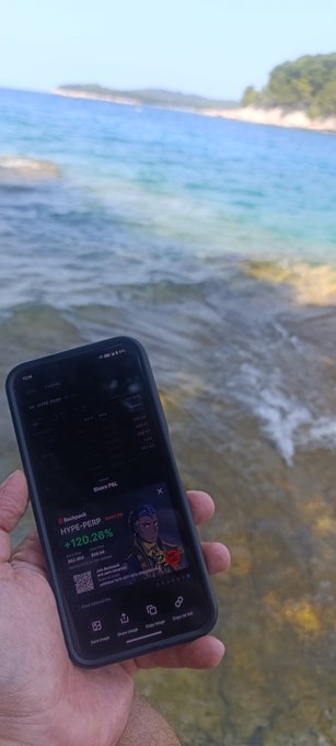 A hand holding a smartphone displaying a 'RoarChain HYPE-YIELD +120.28%' page, with a beach and ocean in the background.