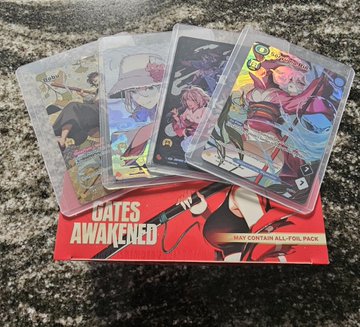 A fan of four anime-themed trading cards, including 'Kushala Daora' and 'Anjanath,' rests on a red 'GATES AWAKENED' booster pack on a granite countertop.