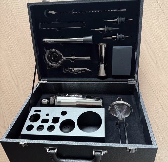 The image features a black leather briefcase with various cocktail shakers, strainers, and other tools inside of it. The briefcase appears to be open, showcasing its contents for inspection. The objects are arranged neatly within the case, suggesting that they are well-organized and ready for use in creating cocktails or other mixed drinks.