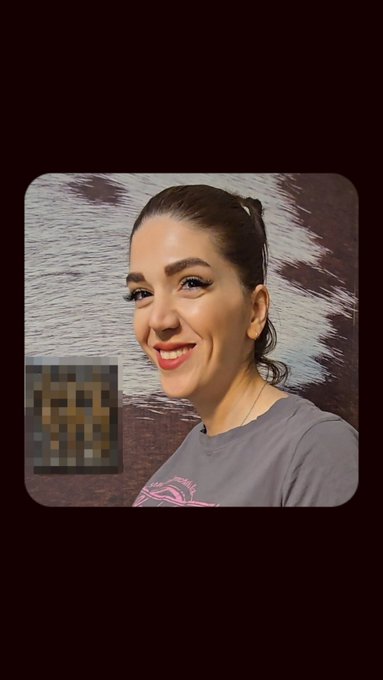 A woman with dark hair and bright blue eyeliner smiles at the camera, with a small blurred image of a dog in the lower left corner.