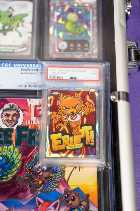 A PSA-graded 2023 Topps Chrome Veefriends "Erupt!" Cynical Cat card (#15) is displayed prominently in a graded slab, surrounded by other Veefriends character cards including those featuring a frog and a smiling character with a cap, all resting on a colorful Veefriends-themed surface.

The image showcases the user's featured card—the fiery Cynical Cat "Erupt!"—as a direct response to the call for favorite collection cards, with its PSA Mint 9 grade highlighting it as a prized piece.