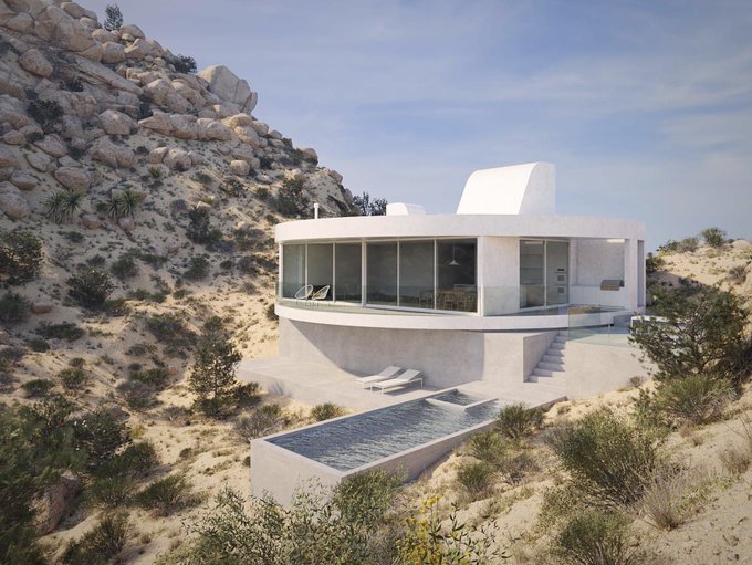 A modern, circular white house with large glass windows is nestled into a desert hillside, featuring an infinity pool and lounge chairs on its terrace.
