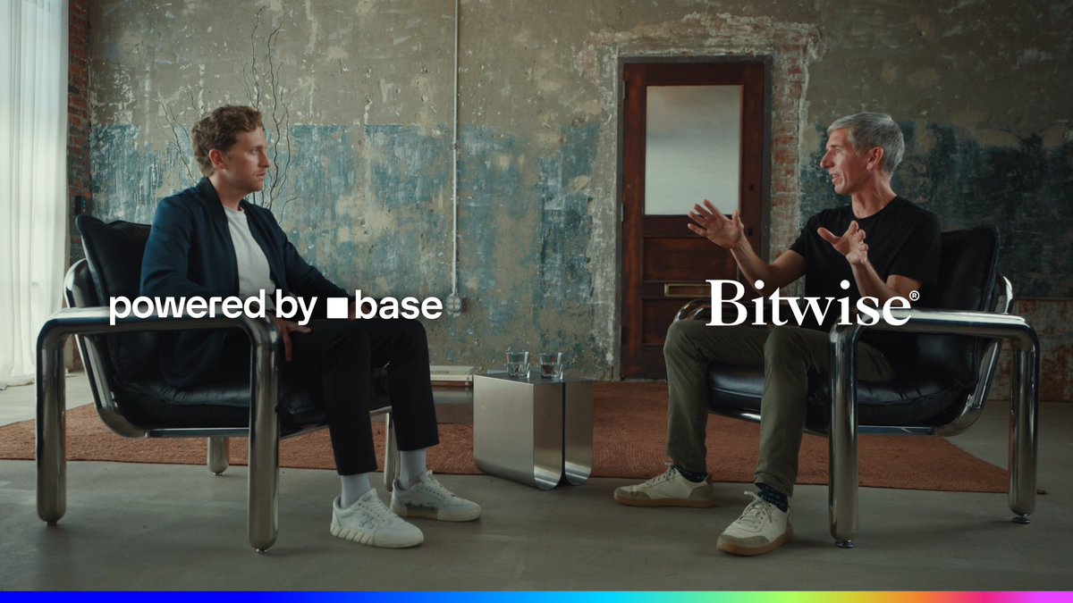 Two men sit in modern black chairs in an industrial-style room with exposed brick walls, engaged in what appears to be a discussion, with one gesturing animatedly. The text "powered by ■ base" appears on the left and "Bitwise®" on the right, with a colorful gradient bar at the bottom—suggesting this is a promotional still for a Bitwise video discussing tokenized stocks as a major innovation in asset management.
