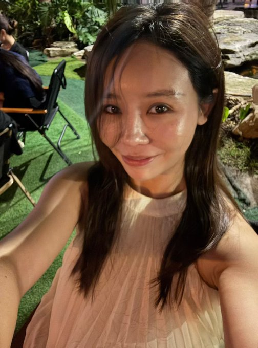 A woman in a peach sleeveless top smiles for a selfie in an outdoor garden setting, her youthful appearance reflecting the post's mention of being 48 years old and an active Binance senior team leader sharing industry insights and personal trading experiences across multiple social platforms.