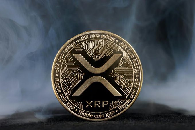 A gold XRP/Ripple coin is displayed against a smoky, dark background with the text 'Ripple coin XRP' inscribed around its edge.