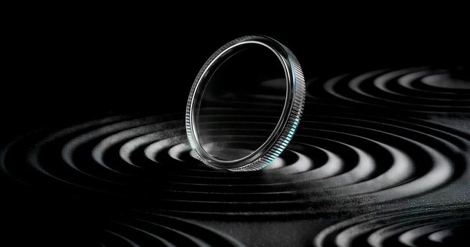 A close-up product shot features a silver ring resting on a black surface with a hypnotic, concentric circle pattern.