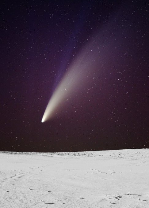 A stunning view of a bright comet with a long, glowing tail streaking across a starry night sky above a snow-covered, textured ground.