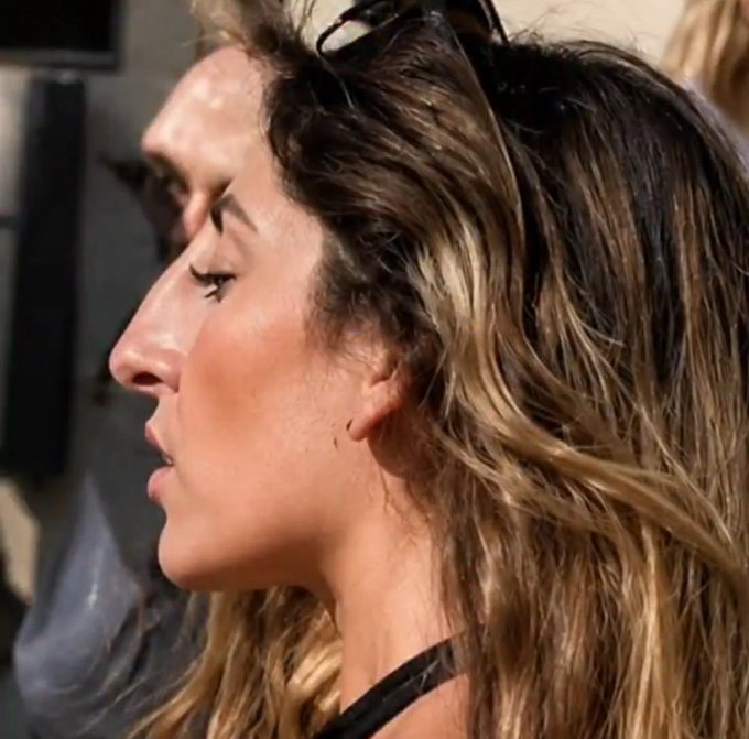 A close-up profile photo of a woman with long, highlighted brown hair, wearing sunglasses on top of her head, with visible makeup including eyeliner and mascara.