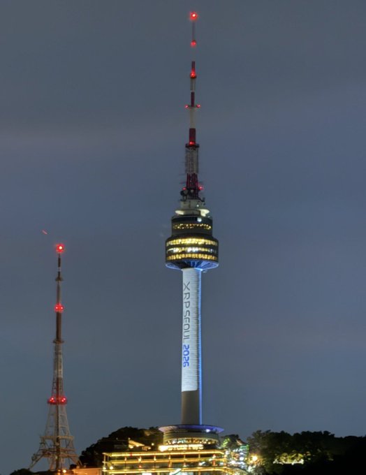 The N Seoul Tower is illuminated at night against a dark sky, with 'XDP SEOUL 2025' projected on its central column.