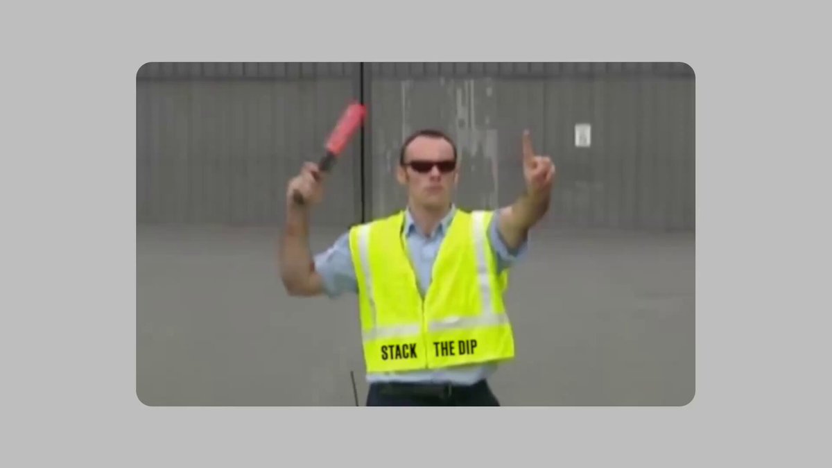 The image features a man wearing a yellow safety vest, holding a red baton or stick with "Stack The Dip" written on his shirt. He appears to be making a peace sign with one hand while pointing with the other. The background of the image is gray and white, which contrasts with the vibrant colors of the man's outfit and the red object he holds.