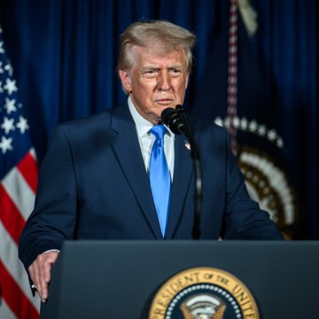 A man, identified as Donald Trump based on the accompanying post context, stands at a podium with the presidential seal, looking downward while addressing an audience, with an American flag visible in the background. The image accompanies news of him announcing the formation of an "AI Force" and an AI "Czar," claiming AI could comprise up to 25% of the country's GDP.