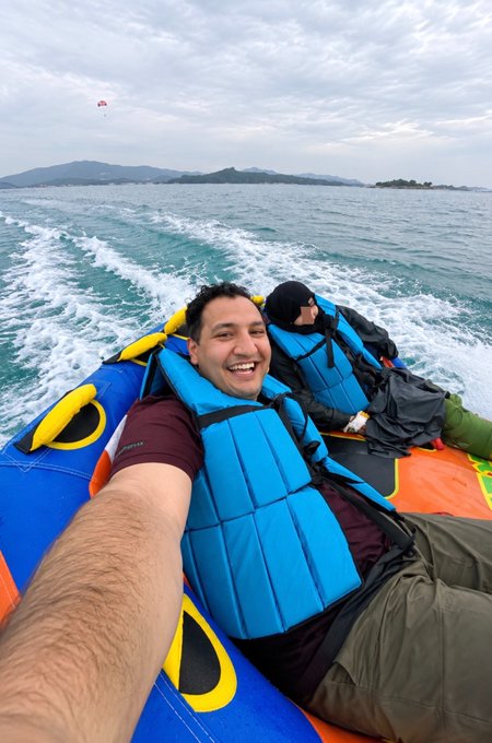 A man smiles broadly while taking a selfie on a colorful inflatable boat, gliding across open water with a coastline visible in the distance. The image perfectly captures the post's message of inner peace and emotional detachment—his relaxed, joyful expression on what appears to be a leisurely boat ride reflects the calmer, more grounded mindset that comes from learning not to let external highs and lows (whether crypto swings or life's turbulence) disrupt his happiness.