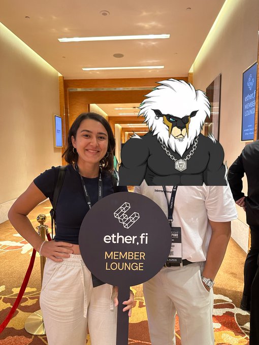 A woman poses with a person wearing an anthropomorphic bird mascot head; they hold a circular sign reading 'ether.fi MEMBER LOUNGE' at what appears to be a conference.