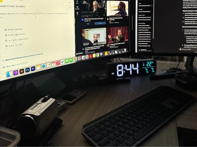 A late-night workspace shows a trading/study setup with a digital clock reading 8:44 and 22°/71° humidity, multiple monitors displaying a Zoom call and a multiple choice question ("as, or g it its right version"), alongside a keyboard and webcam—suggesting the trader is grinding through research or coursework during off-hours while monitoring potential plays.