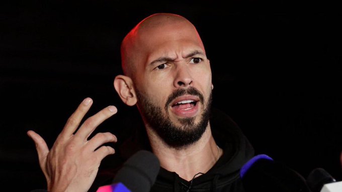 Close-up photo of a bald man with a beard speaking passionately to microphones, gesturing with his hand raised.