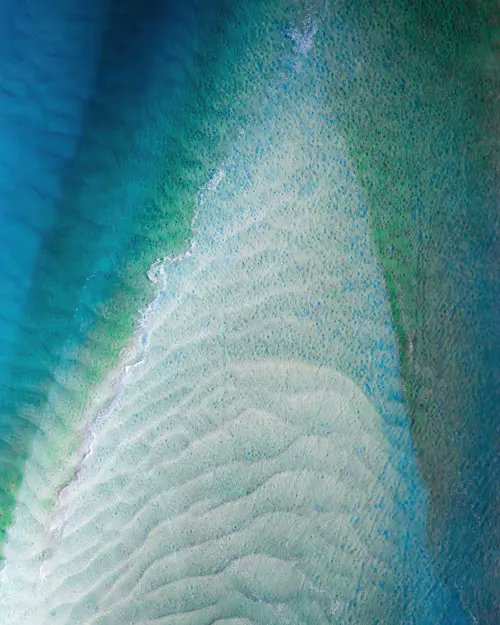 Aerial view of a shallow sandy shoal or reef surrounded by turquoise and deep blue water.
