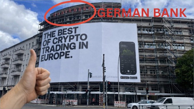 A street view of a building under construction with a billboard advertising 'THE BEST OF CRYPTO TRADING IN EUROPE' with a thumbs-up in the foreground, and red text 'GERMAN BANK' overlaid with a circle.
