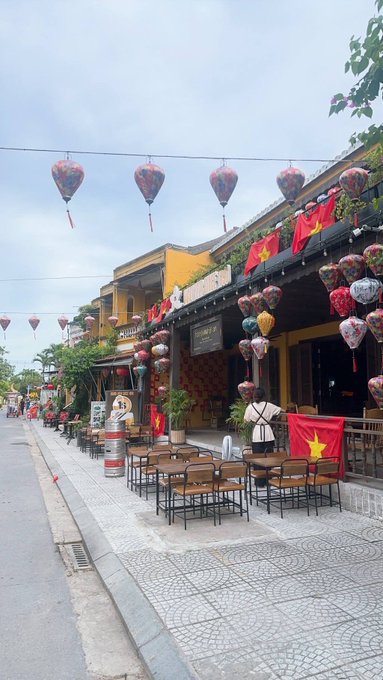 iced tea shop with red and yellow lanterns, a Vietnamese flag, and a "Vietnamese Tea" sign on a street lined with trees and buildings.
