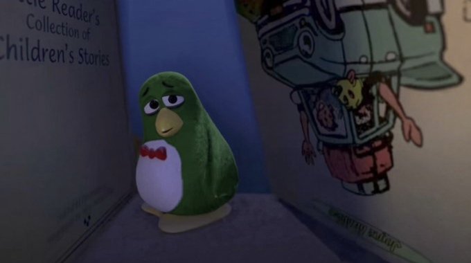 A small sad green penguin figurine with a red bow tie stands between books, with one titled "...Reader's Collection of Children's Stories," gazing longingly at an upside-down children's book illustration—capturing the melancholy mood of a wallet that's seen better days before returning to work.
