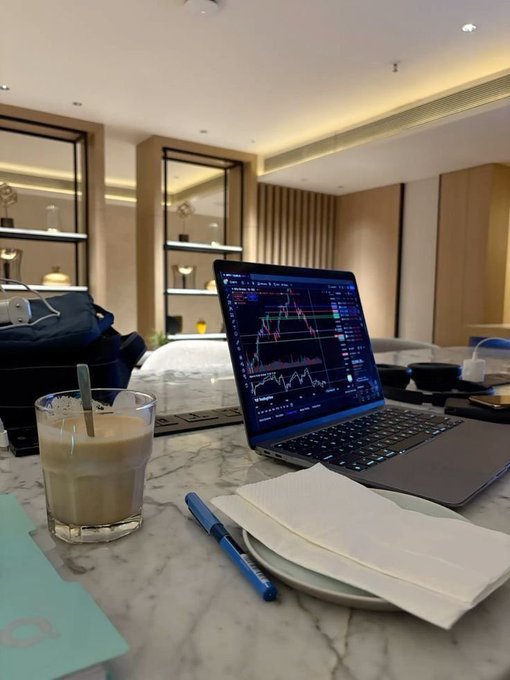 The image shows a laptop computer sitting open on top of a marble table, with a cup of coffee next to it. The scene appears to be set in an office or workspace environment. A book can also be seen placed near the laptop. The caption provided by QuipNetwork suggests that there is a focus on improving infrastructure and usability for blockchain technology, rather than just chasing short term hype.
