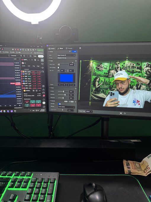A computer desk setup with two monitors displaying video editing and streaming software, a green-backlit keyboard, and a mouse.