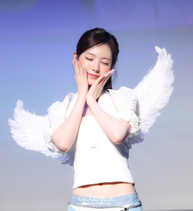 A woman with closed eyes rests her face against her hands, wearing a white outfit with feathered angel wings, set against a blue background with 'CLOUD BLUE' text.