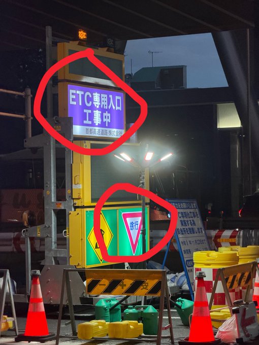 A nighttime photo shows a Japanese construction zone with red circles highlighting a blue sign reading 'ETC専用入口 工事中' (ETC-only entrance under construction) and a green yield sign reading '徐行'.
